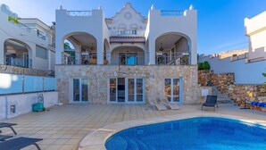 Une villa moderne dotée d’une piscine, d’une façade en pierre et de nombreux balcons.