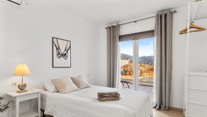 Une chambre à coucher comprenant un lit, une table de chevet, une lampe, un tableau encadré et une vue sur l’extérieur.