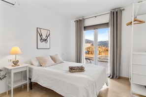 Een slaapkamer met een bed, een nachtkastje, een lamp, een kunstwerk in een lijst en uitzicht op de omgeving.