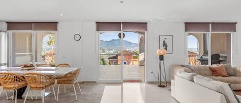 A spacious living area with a balcony, a dining table with chairs, a sofa, and a lamp.