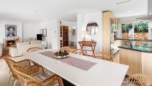 Un salon spacieux avec une cheminée, un coin repas avec des chaises en osier et une cuisine dotée d’un plan de travail en pierre.