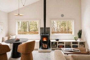 A modern living room with a fireplace, large windows, and a cozy seating area. - Sauna, Hot Tub, Fire Pit & Creekside Deck | Niksen (Callicoon)
