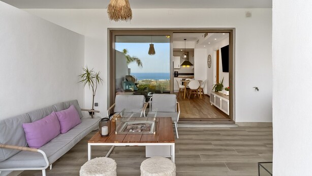 A modern living room with a sofa, coffee table, and ottoman, a dining area with chairs, a kitchen, and a view of the sea. - Private Jacuzzi for Romantic Getaways a221 (Mijas Costa)