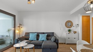 A modern living room with a grey sectional sofa, two white side tables, a glass door leading outside, and a white cabinet with a wicker basket. - Private Jacuzzi for Romantic Getaways a221 (Mijas Costa)