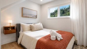 Una camera da letto con un letto, un comodino, una lampada, una finestra con tende e un quadro appeso al muro.