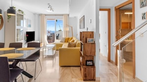 A modern living room with a sofa, dining table, and chairs, a staircase, and a view of the city.