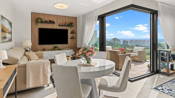 Un salon moderne doté d’un téléviseur à écran plat, de sièges confortables, d’un coin repas et d’une grande fenêtre offrant une vue sur la ville.