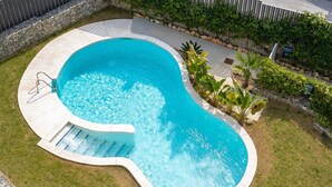 Une piscine à bord incurvé, avec une échelle et un mur de pierre en arrière-plan.