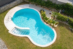 Une piscine à bord incurvé, avec une échelle et un mur de pierre en arrière-plan.