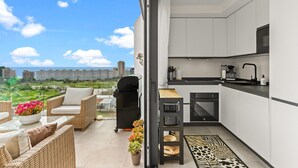 Un balcon agrémenté de meubles en osier, d’un barbecue et de plantes en pot.