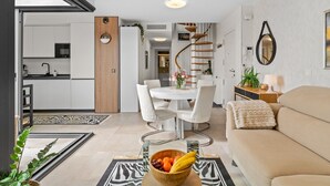 Un salon moderne avec un canapé, une table à manger et des chaises, une cuisine en arrière-plan et un escalier en colimaçon.