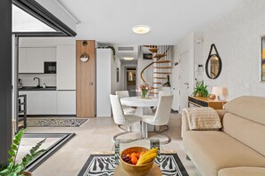 Un salon moderne avec un canapé, une table à manger et des chaises, une cuisine en arrière-plan et un escalier en colimaçon.