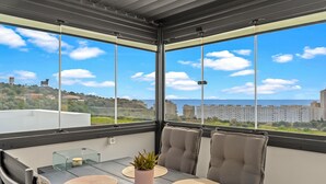Un balcon avec une table, des chaises, un pot de fleurs et une vue sur des bâtiments et de la verdure.