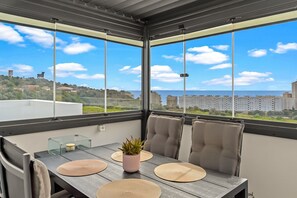 Un balcon avec une table, des chaises, un pot de fleurs et une vue sur des bâtiments et de la verdure.