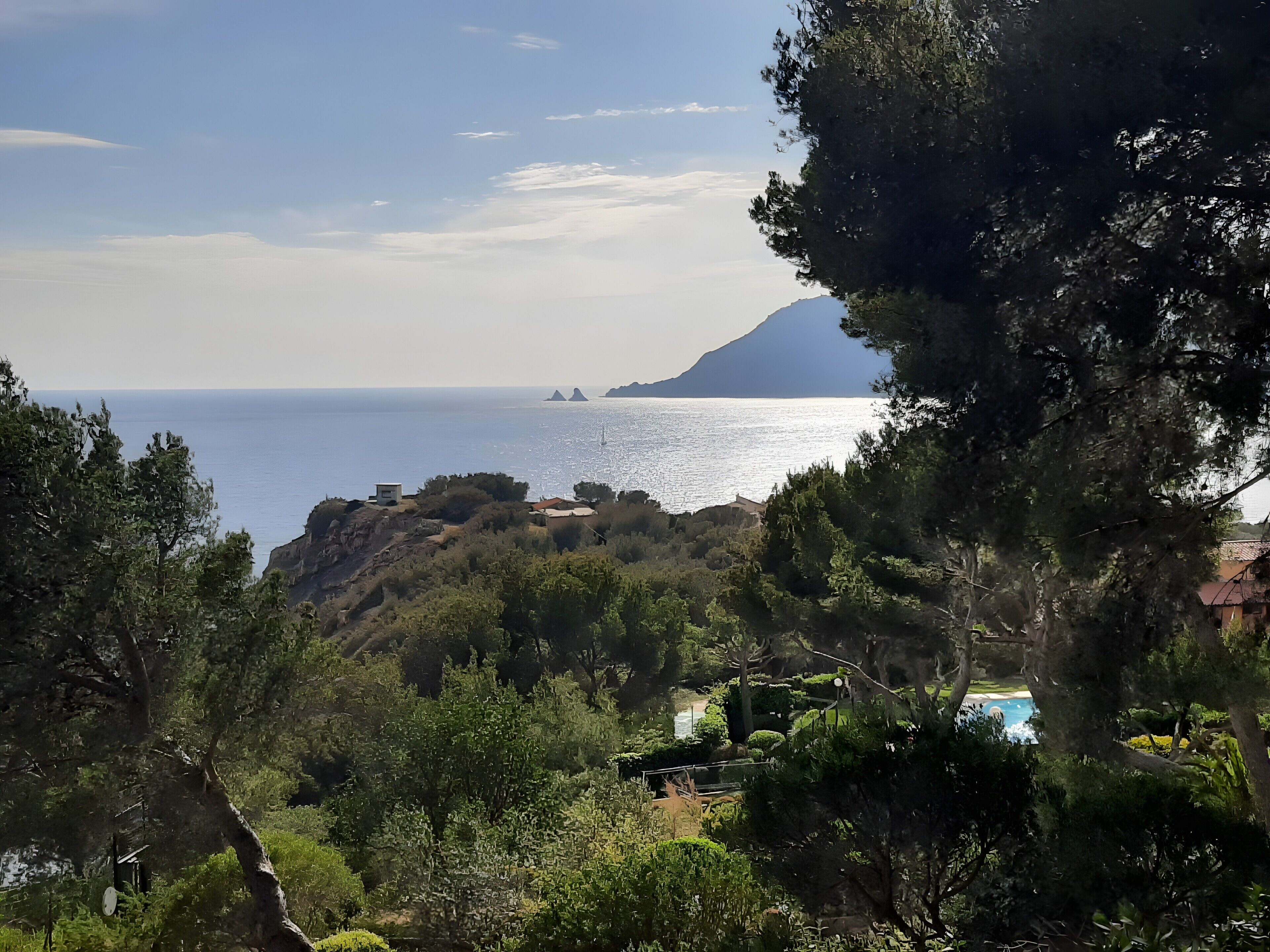 A coastal landscape with a view of the sea, rocky terrain, and dense greenery.