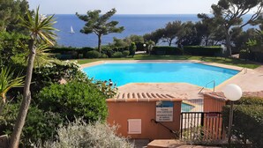 Una piscina con vista al mar, rodeada de vegetación y un letrero que indica ausencia de socorristas.