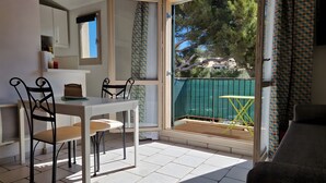 Una habitación con una mesa de comedor, sillas, un sofá y un ventanal corredero que da a un espacio exterior con una cerca verde y árboles.