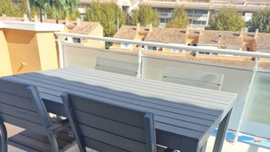 Un balcon avec une table et des chaises en métal, donnant sur un quartier résidentiel avec des maisons et des palmiers.