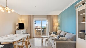 Uma sala moderna com área de refeições, um sofá, uma TV e vista para o exterior.