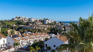 Uma área residencial costeira com edifícios brancos, alguns com painéis solares, e um céu azul límpido.