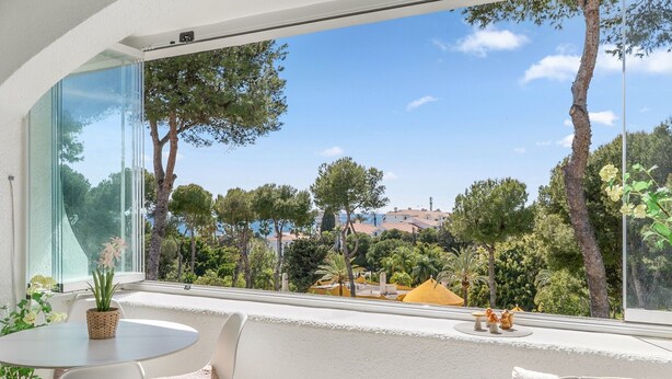 Un balcon donnant sur des arbres et des immeubles, une table ronde avec des chaises et une plante en pot.