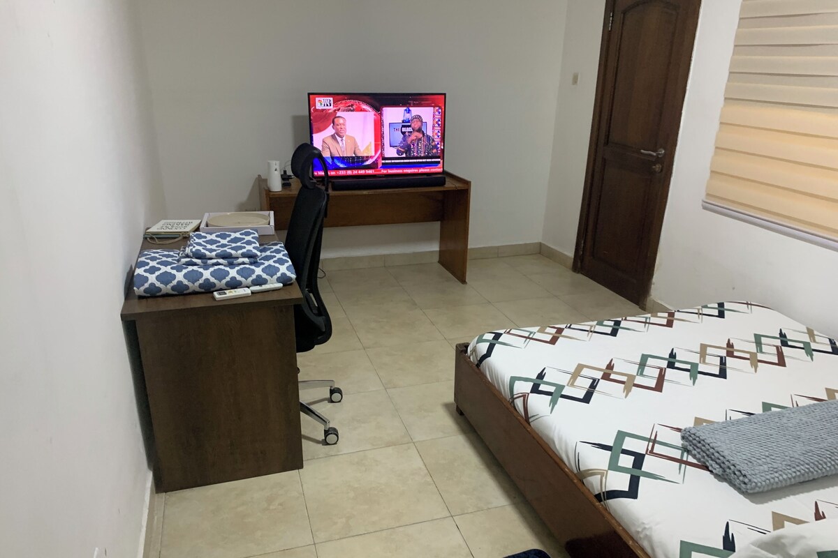 Een slaapkamer met een bed, een bureau met een computer, een stoel en een kledingkast.