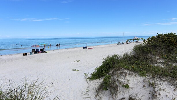 A beach with clear skies, a sandy shore, and a few umbrellas and beach chairs.