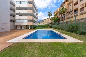 Une piscine à l’eau d’un bleu limpide, entourée d’une pelouse et bordée d’un bâtiment doté de balcons.