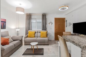 A modern living room with a sofa, a coffee table, a TV, and a kitchen area. - Centrally Located Penthouse with Balcony, Wi-Fi & Air Conditioning in Fuengirola (Fuengirola)