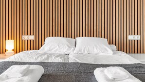 Una habitación de hotel con una cama, ropa de cama blanca, una manta gris y dos toallas blancas sobre la cama.