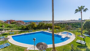 Una piscina con vista al mar, rodeada de palmeras y sillas de descanso.