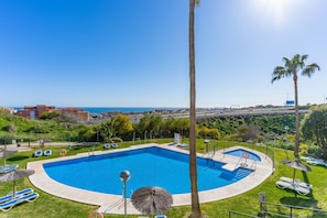 A pool with a view of the sea, surrounded by palm trees and lounge chairs.