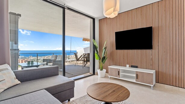 Una sala de estar moderna con un sofá, una mesa de centro, un televisor y un ventanal con vistas al mar.