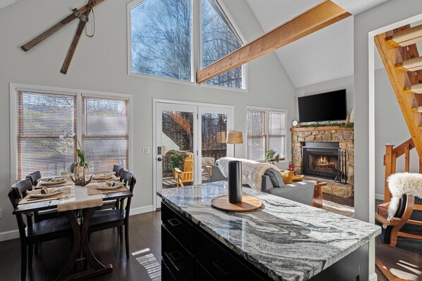 A spacious living area with a large stone fireplace, a dining table set for six, and a high ceiling with exposed beams.