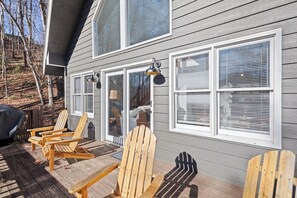 A wooden deck with Adirondack chairs, large windows with blinds, and a covered grill area.