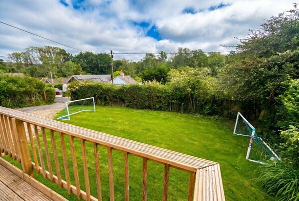 A residential backyard with a wooden deck, a well-maintained lawn, and a soccer goal.