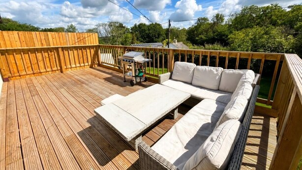 A wooden deck with a white sofa and a grill.
