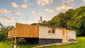 A single-story house with a wooden deck, a chimney, and a small front porch. - Family-friendly countryside home with hot tub, swing set and trampoline (Battle)