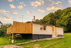 Une maison de plain-pied avec une terrasse en bois, une cheminée et un petit porche à l’avant.