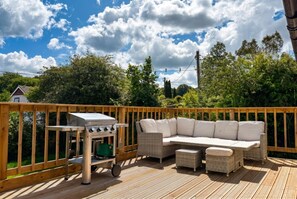 A deck with outdoor furniture, a grill, and a view of the surrounding greenery.