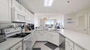 Una cucina moderna con mobili bianchi, forno a microonde, piano cottura e lavastoviglie integrati. Un'ampia finestra offre luce naturale e vista sull'esterno.