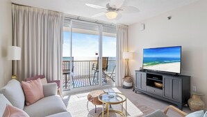 Un soggiorno con divano, TV e un balcone vista spiaggia.