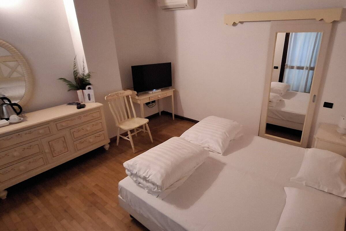 Une chambre d’hôtel avec un lit, une télévision, une commode, une chaise et un miroir.
