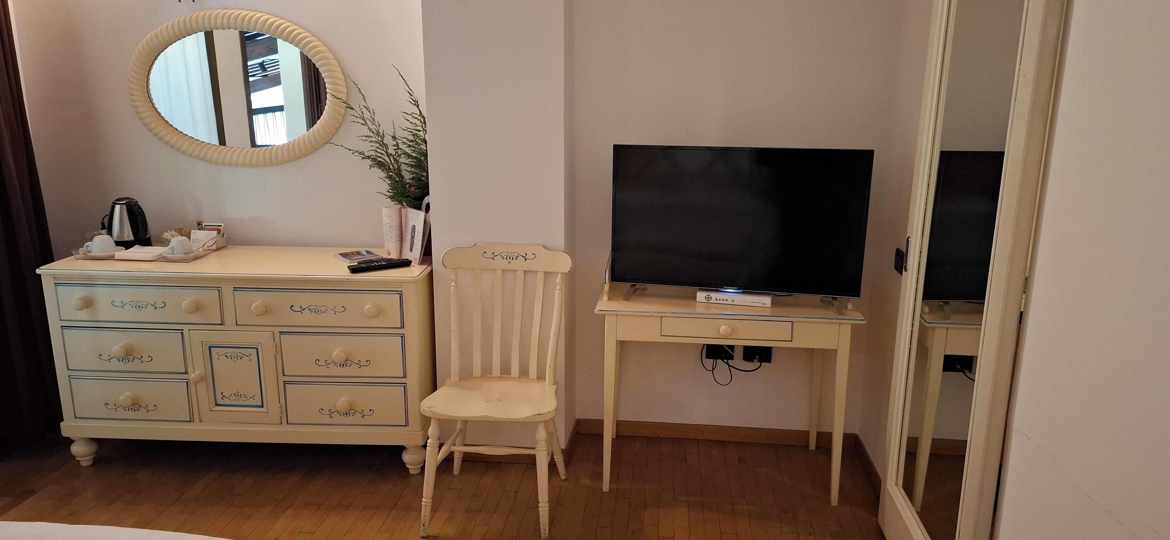A room with a wooden dresser with drawers, a mirror, a television on a stand, and a chair.