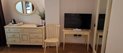 A room with a wooden dresser with drawers, a mirror, a television on a stand, and a chair.