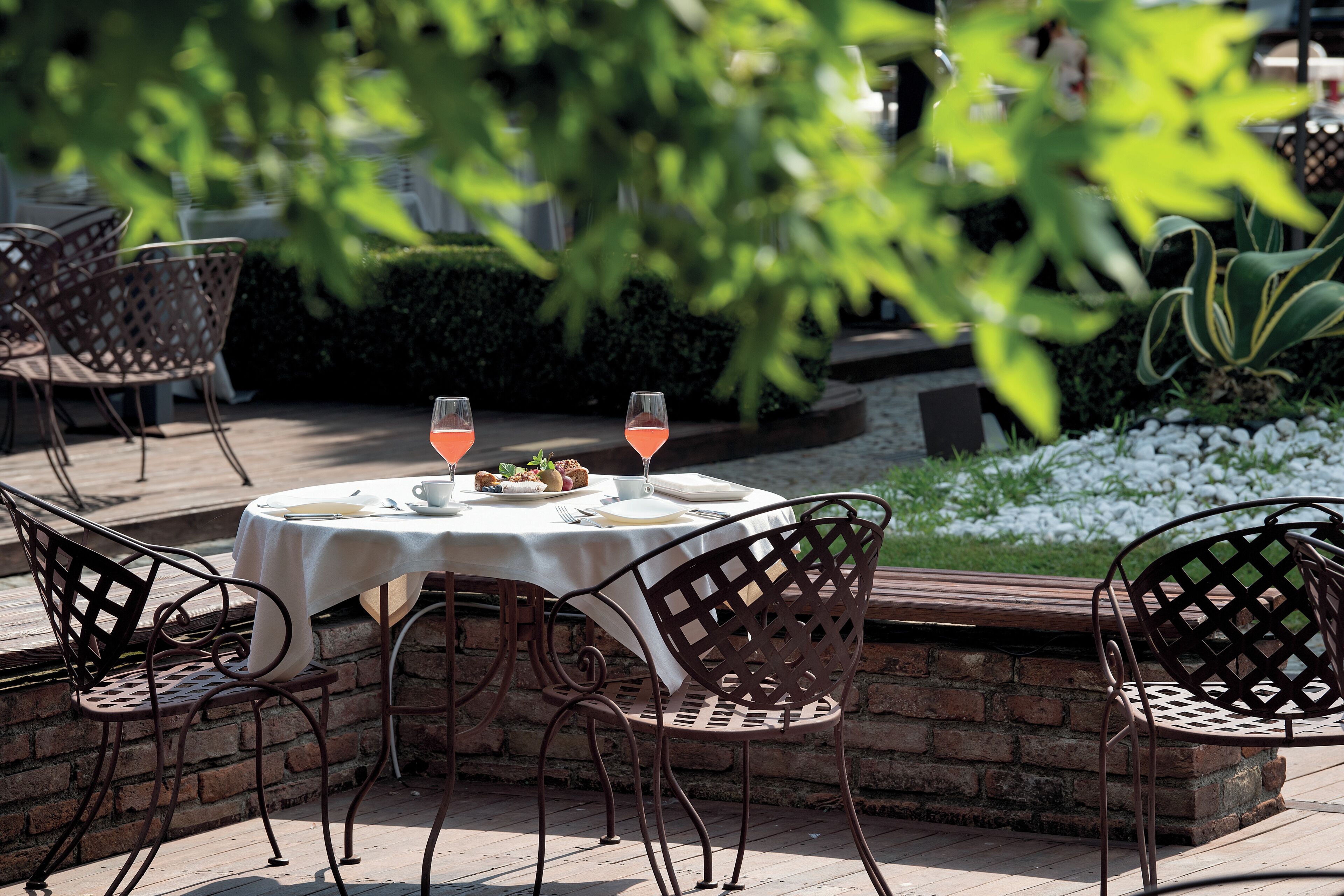 An outdoor dining area with a round table, four chairs, and two glasses of pink beverage.