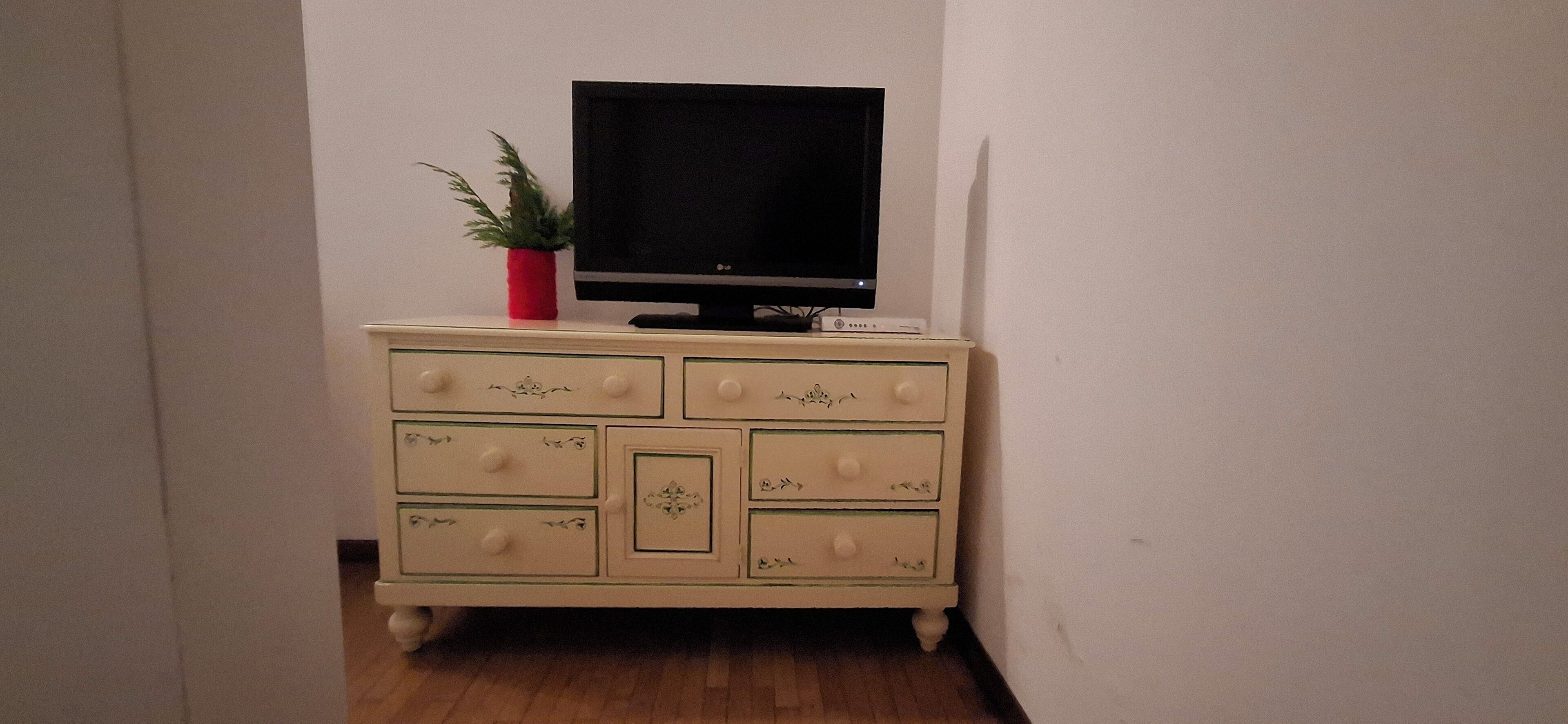 Uma cômoda cor de creme com gavetas e uma televisão em cima.