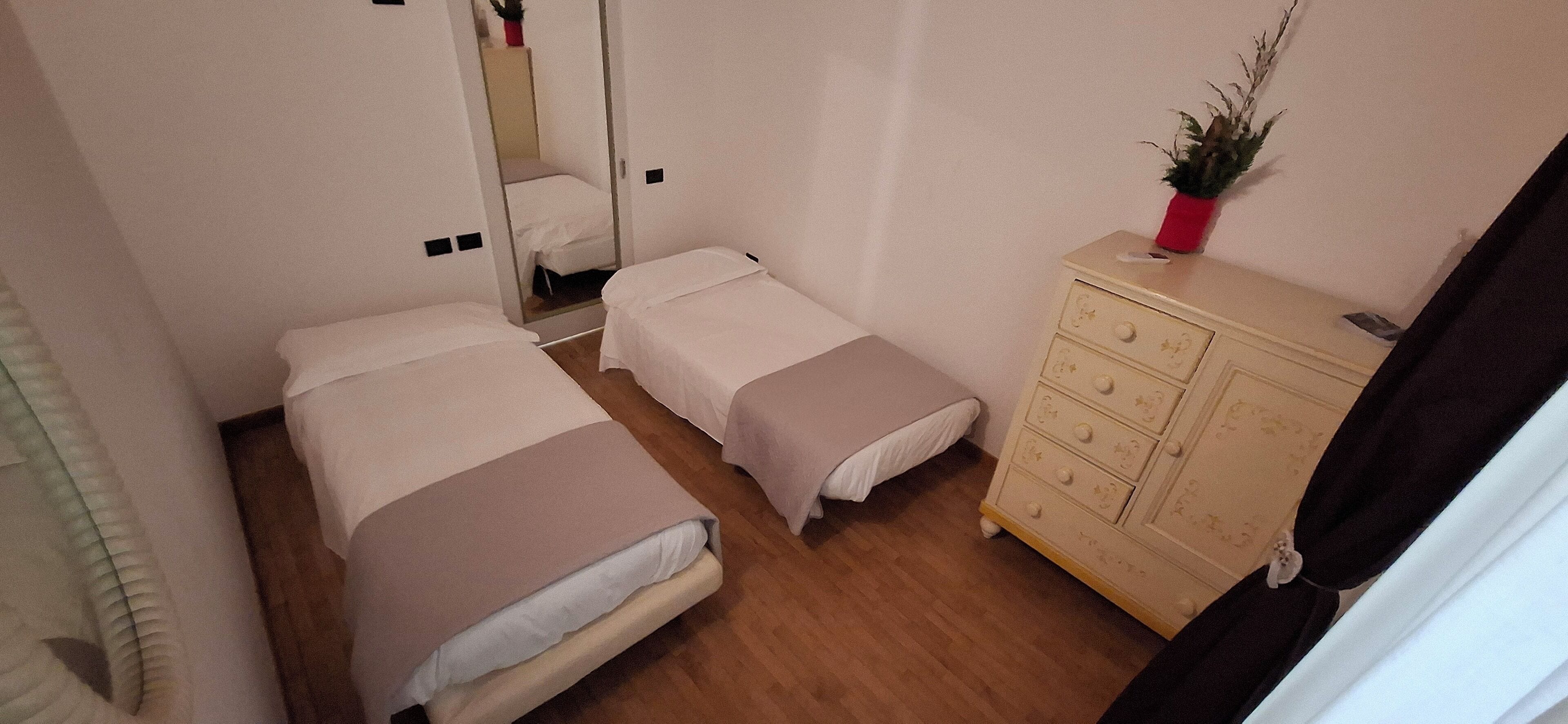 A small, compact bedroom with two single beds, a wooden dresser, and a mirror.