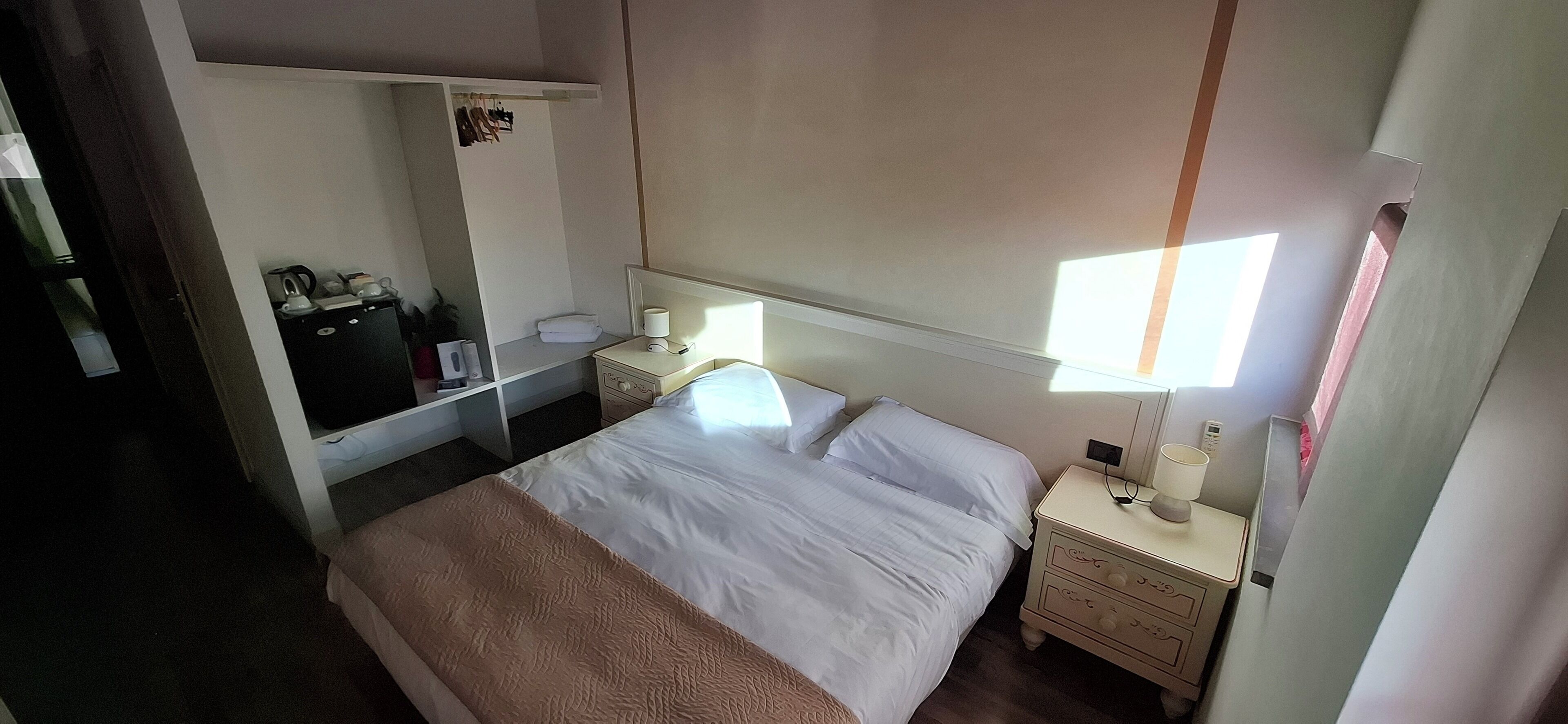 Ein ordentlich eingerichtetes Hotelzimmer mit Bett, Nachttischen, einem Kleiderschrank und einem Spiegel.