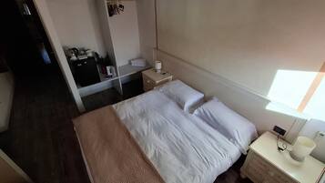 Een hotelkamer met een bed, nachtkastje, lamp en een klein bureau met stoel.